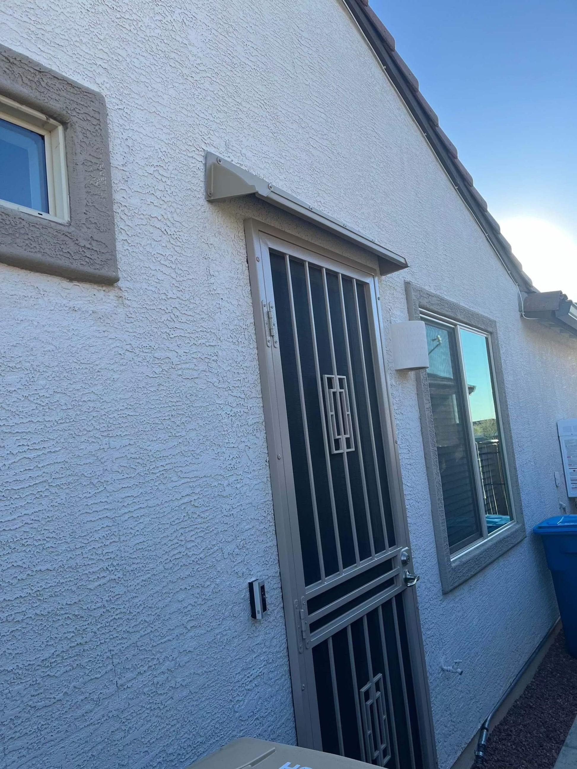 A beige storm door rain guard mounted above a screen door.
