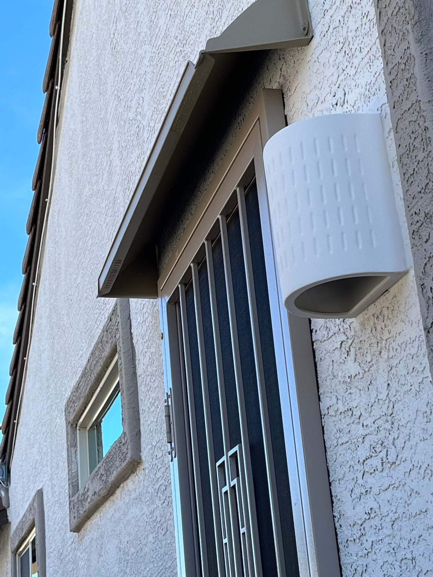 A beige storm door rain guard mounted above a screen door.
