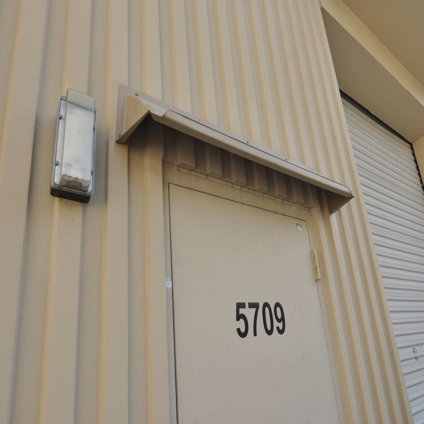 Beige rain diverter mounted on vertical ribbed tilt building.