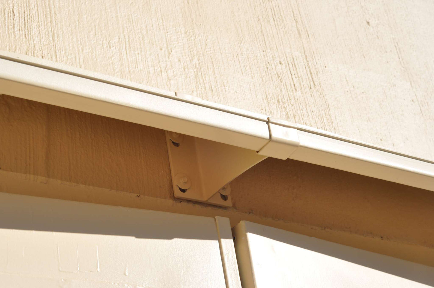 Looking up at a DOORBRIM electric service rain diverter or hood and splice bracket above two exterior doors.