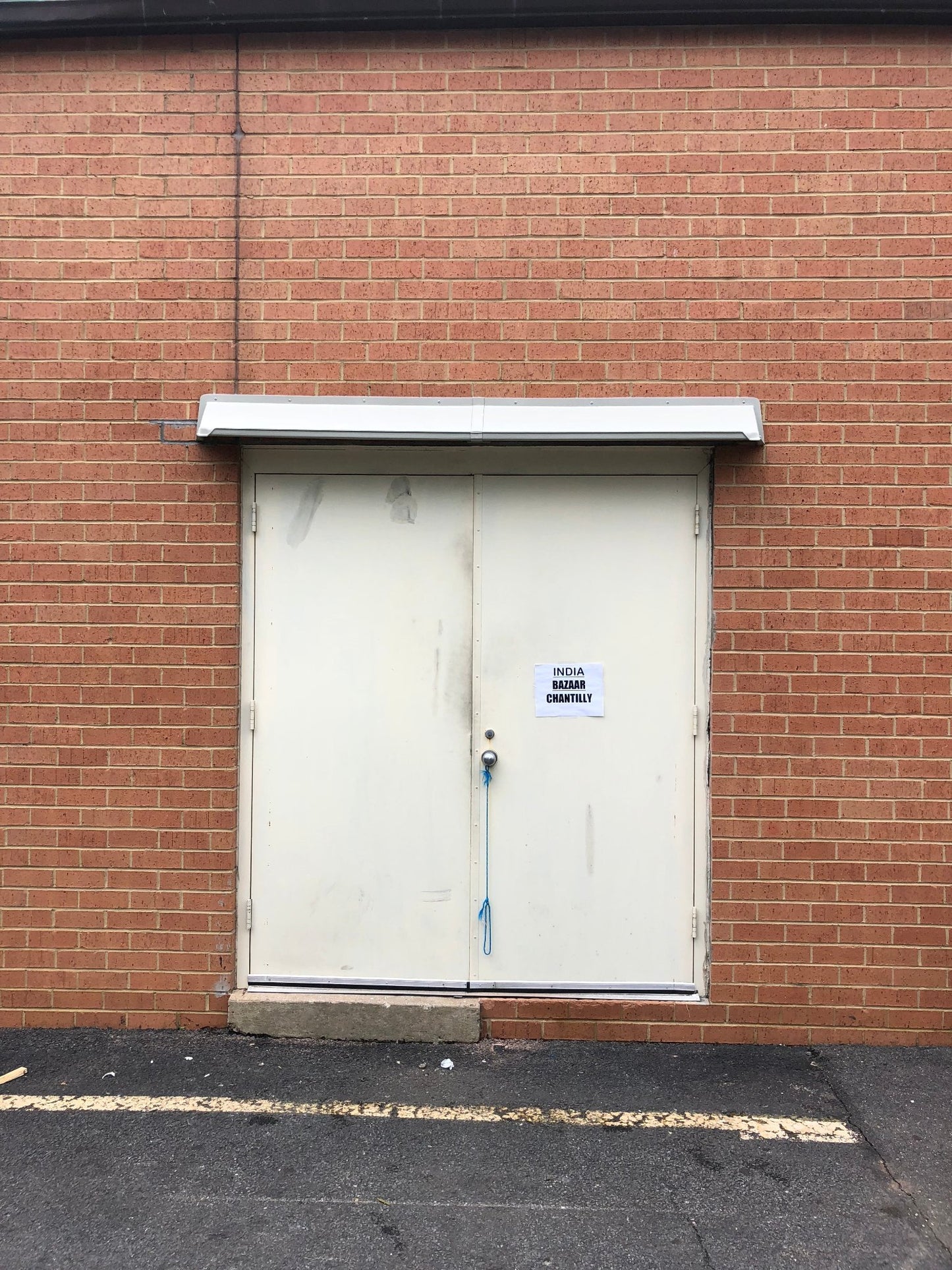 Off white DOORBRIM door canopy mounted above double solid hollow metal doors in a red brick building.