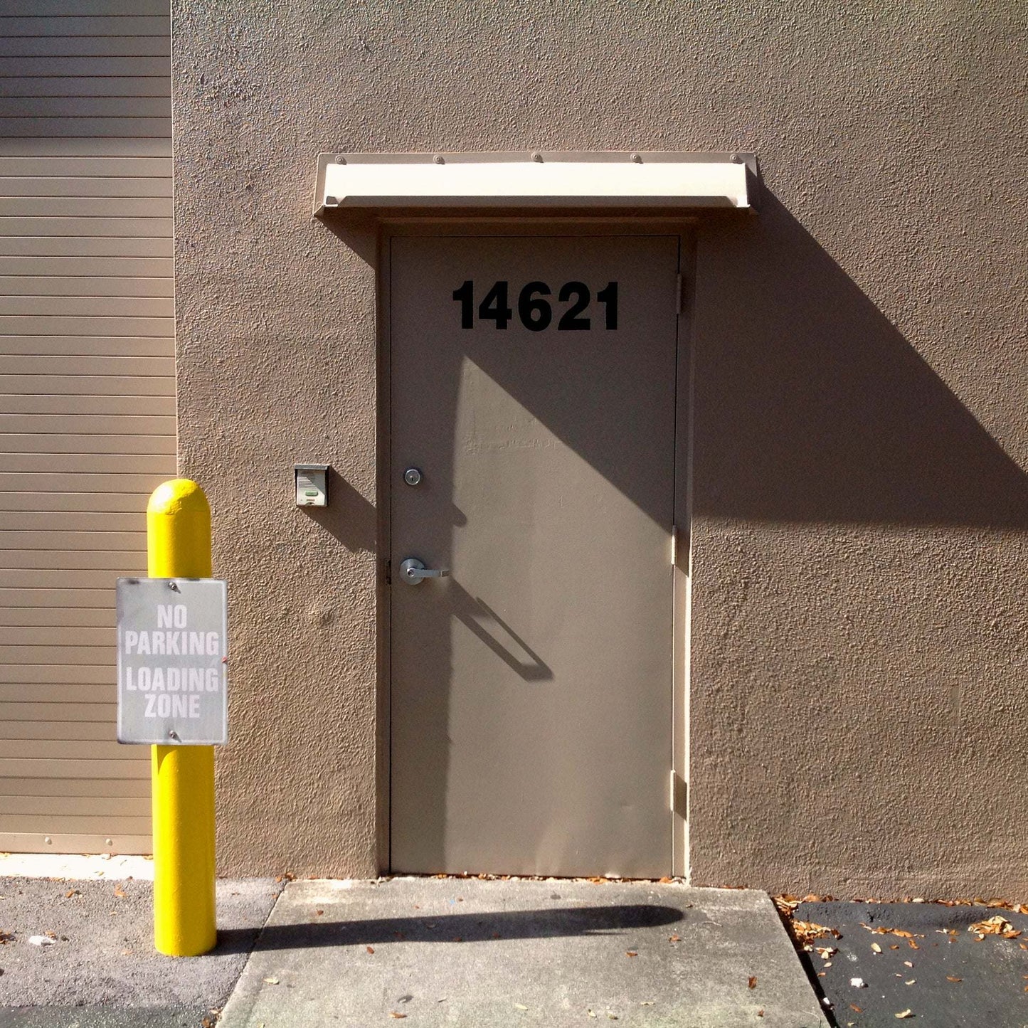 Beige rain diverter mounted above a single hollow metal door in a warehouse.