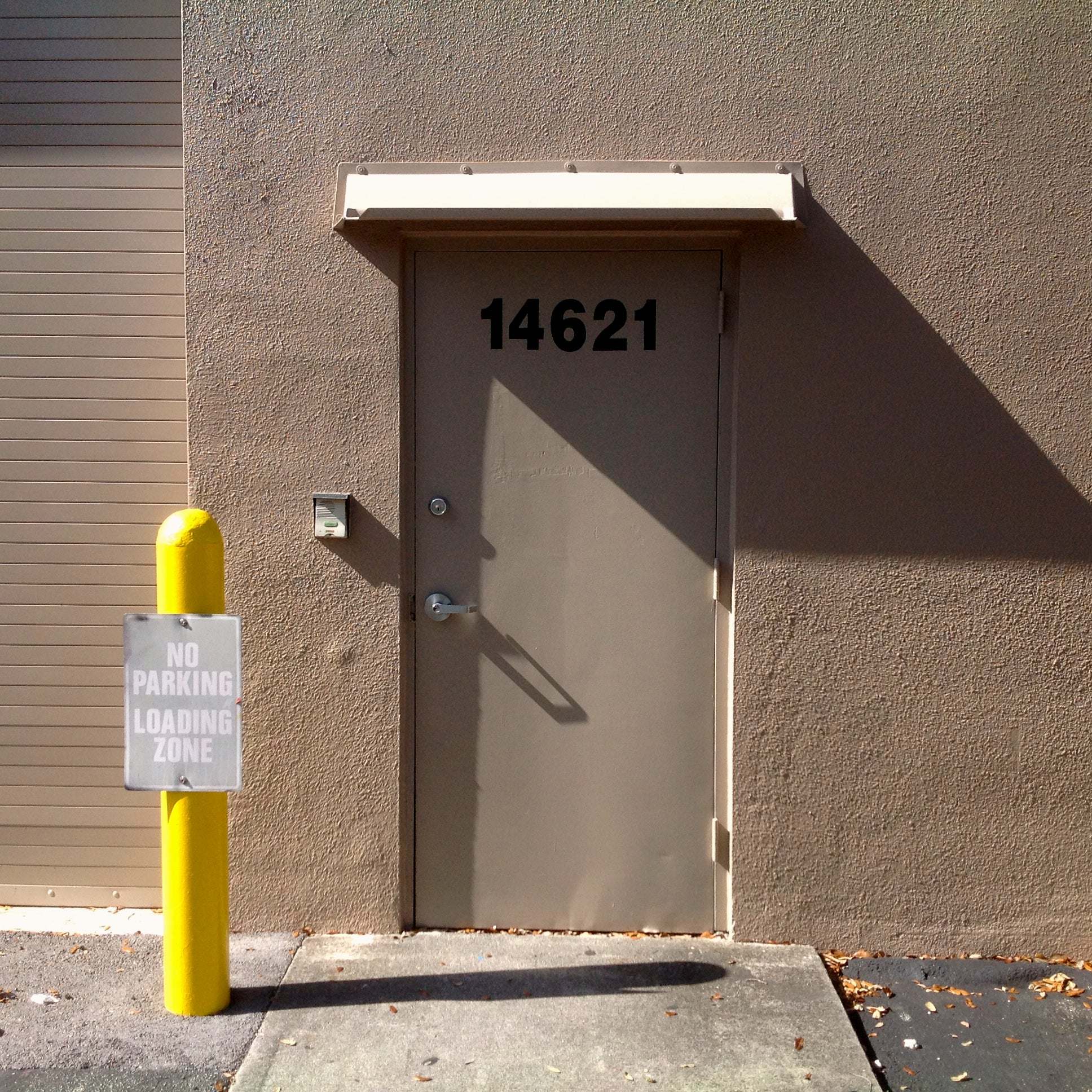 Beige rain diverter mounted above a single  hollow metal door in a warehouse.