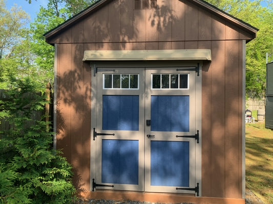 A brown shed is shown with blue double doors, cream color trim and a DOORBRIM rain hood mounted above.
