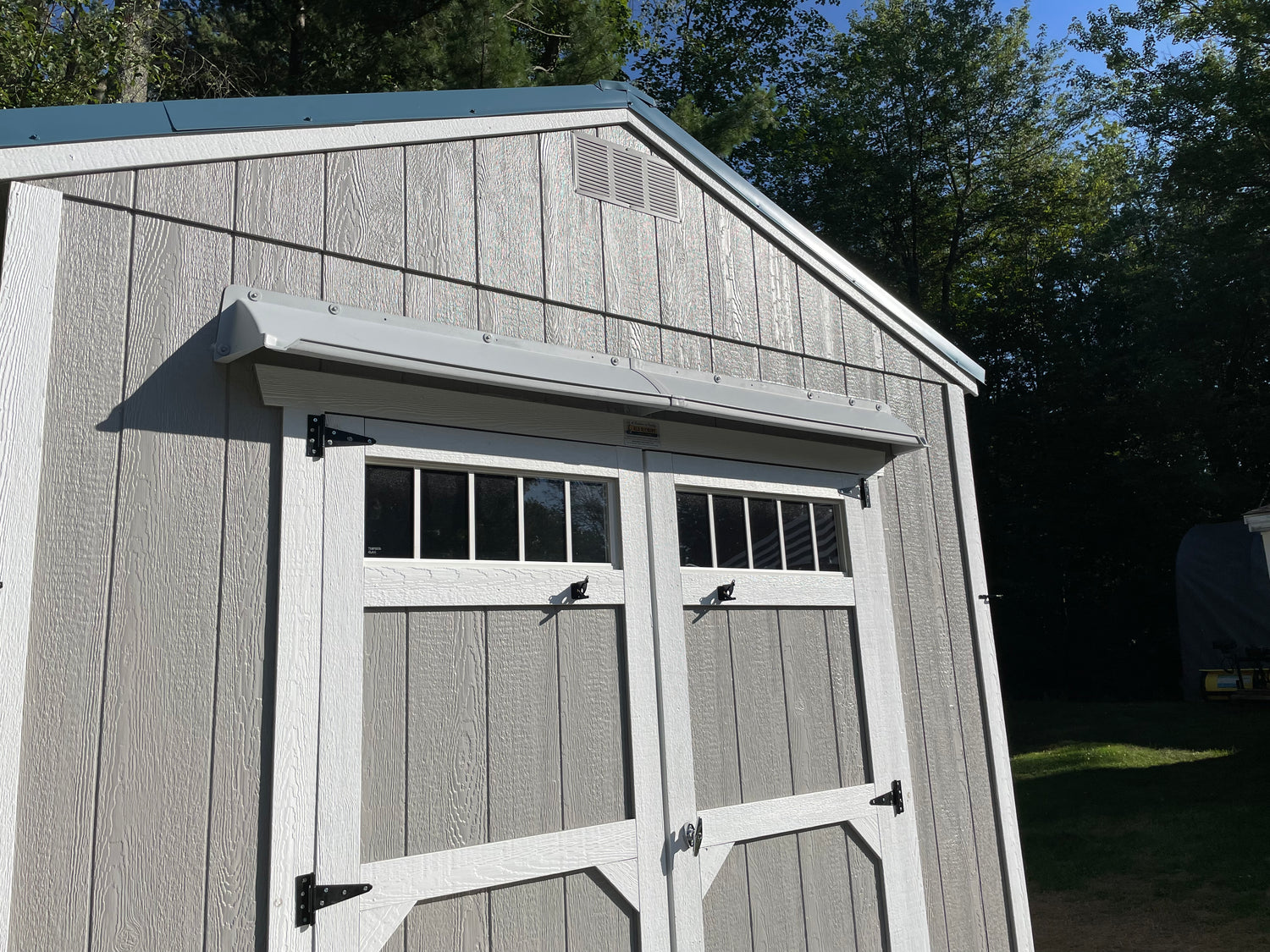 Gray and white shed with a gray rain diverter mounted above double doors.
