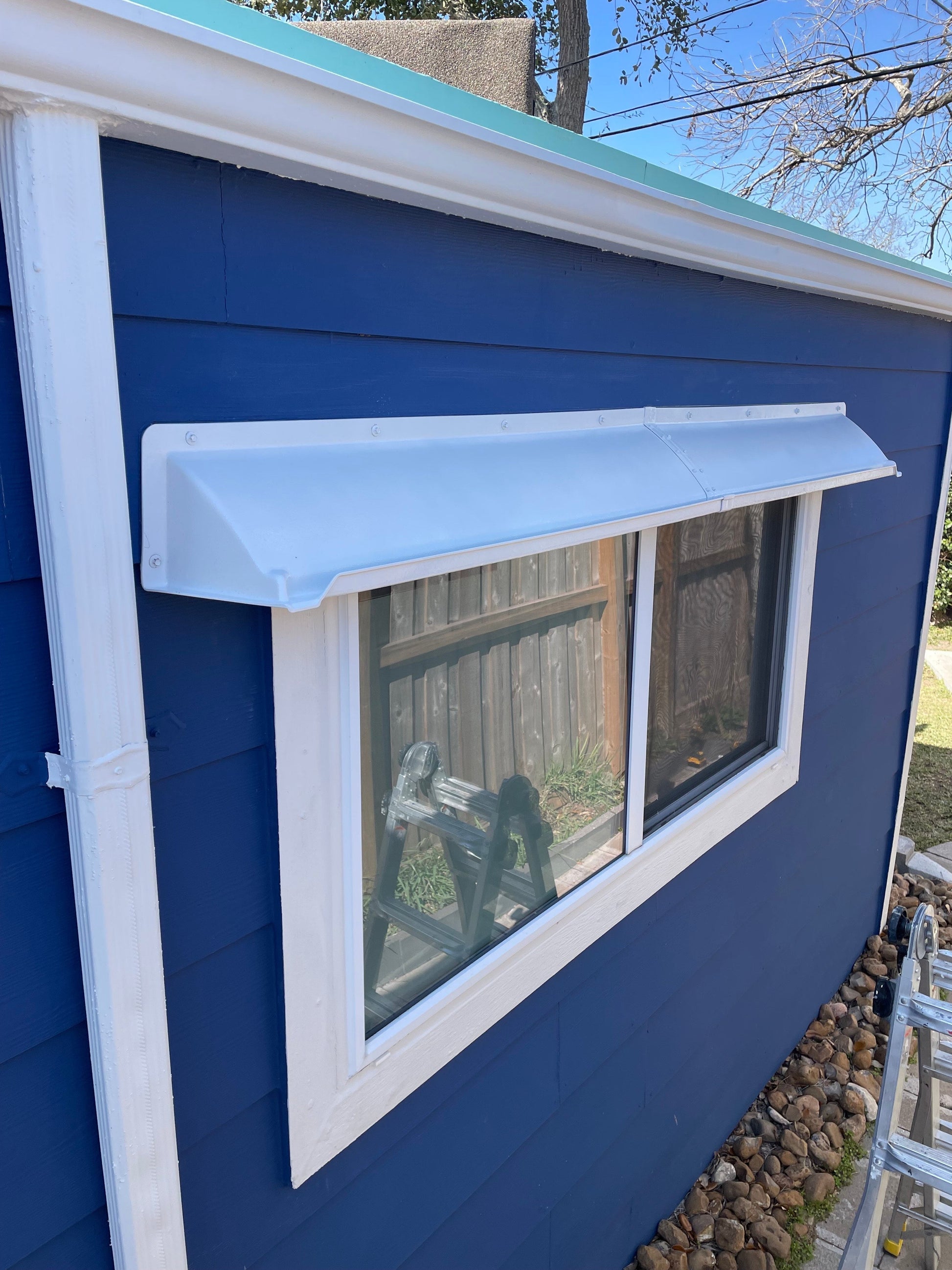 Extended width rain guards for house windows installed above white siding to prevent water leaks