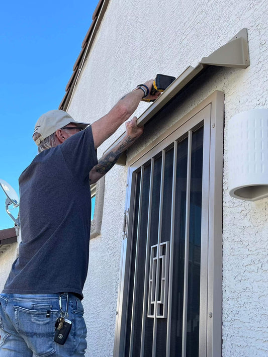 Man on ladder mounting a beige storm door rain guard above door.