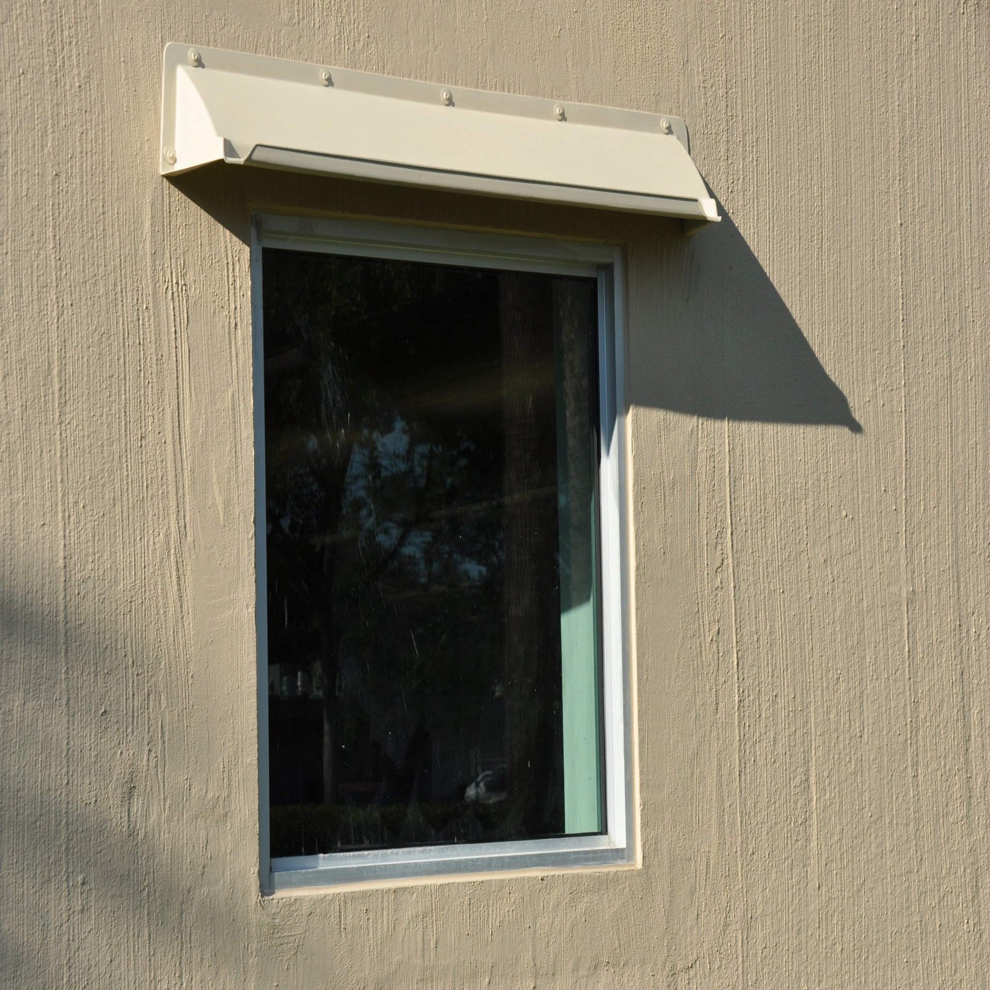 Beige rain diverter mounted above a fixed panel single window in a tilt building.